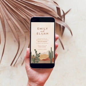 May include: A mobile phone screen displaying a wedding invitation for Emily and Elijah. The invitation features a desert landscape with cacti and mountains in shades of brown, orange, and green. The text reads "Emily and Elijah are getting married, please join us to celebrate, 28-07-2024, 5 o'clock in the afternoon, Tongue Verde Ranch, Tucson, Arizona, reception to follow."