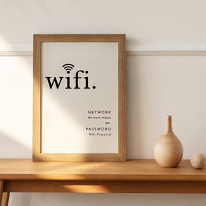 May include: A framed print with the word "wifi" in black, along with fields for network name and password. A small wooden vase and ball sit on a wooden surface. The frame is a light brown color.