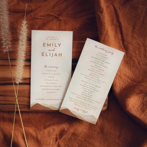 May include: Wedding ceremony program with a rustic theme. The program features a light brown background with a tan and orange mountain range design. The text is in a brown font and includes the names Emily and Elijah, the wedding date, and the ceremony order.