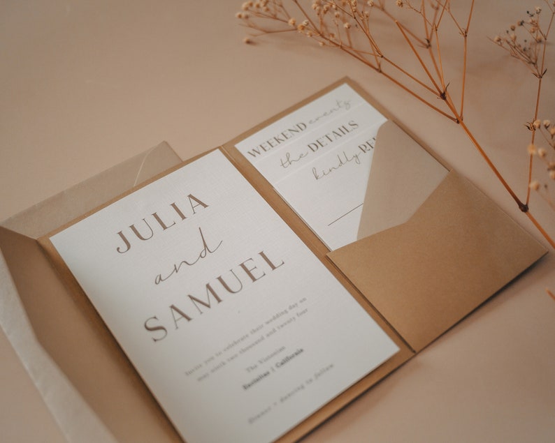 Pu&ograve; includere: Un invito di nozze piegato con una busta marrone. Il fronte dell'invito &egrave; bianco con il testo "JULIA e SAMUEL" in un carattere minimalista.