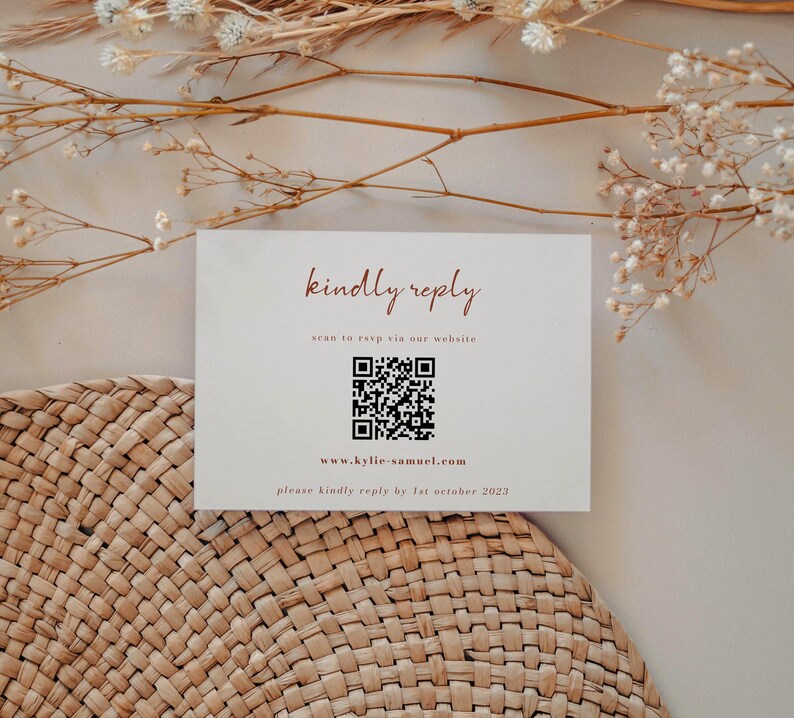 May include: A white card with the text "kindly reply" in brown cursive. Below the text is a QR code with the text "scan to rsvp via our website" and the website address "www.kylie-samuel.com". The text "please kindly reply by 1st october 2023" is at the bottom of the card.