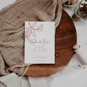 May include: A minimalist wedding invitation with a brown line drawing of a leafy branch. The text reads "Kayla & Eric" and includes the date "JAN 12 2023" and the location "byron tides estate byron bay | new south wales".