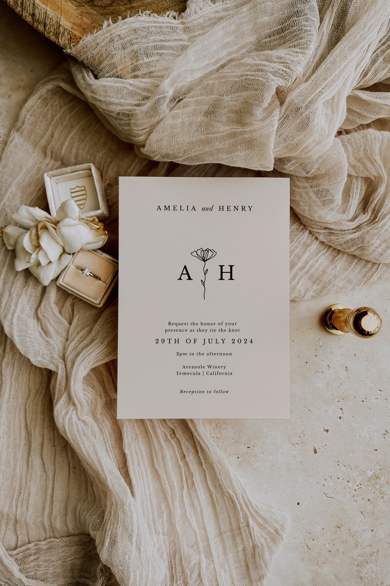 K&ouml;nnte beinhalten: Hochzeitseinladung mit beigefarbenem Hintergrund und schwarzem Text. Die Einladung lautet "Amelia und Henry" mit einem floralen Design und den Initialen "AH". Das Datum der Hochzeit ist der 29. Juli 2024, und der Ort ist Avensole Winery in Temecula, Kalifornien.
