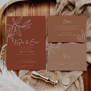 May include: A rustic wedding invitation suite with a brown background and white floral illustrations. The invitation features the couple's names, "Kayla & Eric", and the wedding date, "Jan 12, 2023". The details card includes the venue, "Byron Tides Estate, Byron Bay, New South Wales", and the website, "www.kayla-eric.com". The RSVP card includes the options to accept or regret, with a request to reply by October 1st, 2023.