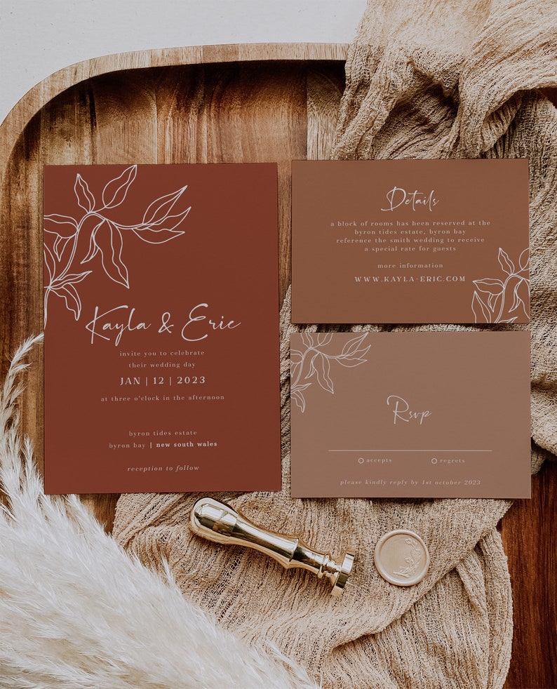 May include: A rustic wedding invitation suite with a brown background and white floral illustrations. The invitation features the couple's names, "Kayla & Eric", and the wedding date, "Jan 12, 2023". The details card includes the venue, "Byron Tides Estate, Byron Bay, New South Wales", and the website, "www.kayla-eric.com". The RSVP card includes the options to accept or regret, with a request to reply by October 1st, 2023.