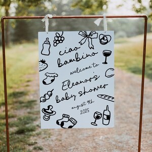 Op de afbeelding: Een wit bord met zwarte doodle-illustraties en de tekst "ciao bambino welcome to Eleanor's baby shower august 9th 2025".