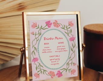 May include: A gold-framed menu card with a pink background and floral design. The menu lists beer, wine, and cocktails. The text "Drinks Menu" is at the top. The card is displayed on a wooden surface.