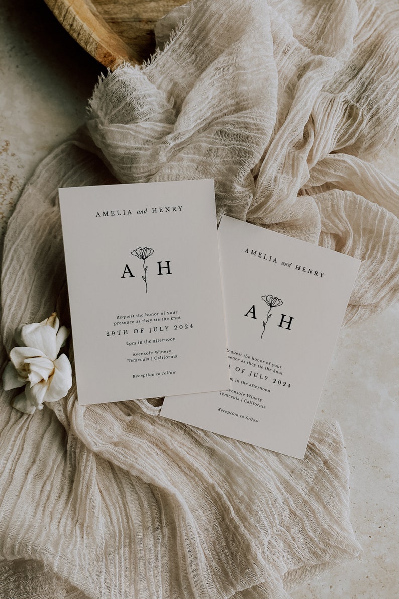 K&ouml;nnte beinhalten: Zwei wei&szlig;e Hochzeitseinladungen mit schwarzem Text und einem schlichten Blumenmuster. Die Einladungen k&uuml;ndigen die Hochzeit von Amelia und Henry am 29. Juli 2024 um 14:00 Uhr im Avensole Winery in Temecula, Kalifornien, an.