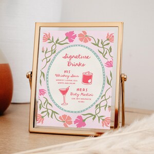 Puede incluir: Un letrero con marco dorado con fondo rosa muestra "Signature Drinks". Enumera "His" Whiskey Sour y "Hers" Dirty Martini, con ilustraciones de c&oacute;cteles. Dise&ntilde;os florales y de vid rosas y verdes rodean el texto.