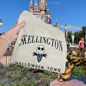 May include: A beige sweatshirt with the text "Jack Skellington Est. 1993 Halloween Town" in black and white embroidery. A black and white embroidered image of Jack Skellington is in the center of the sweatshirt.