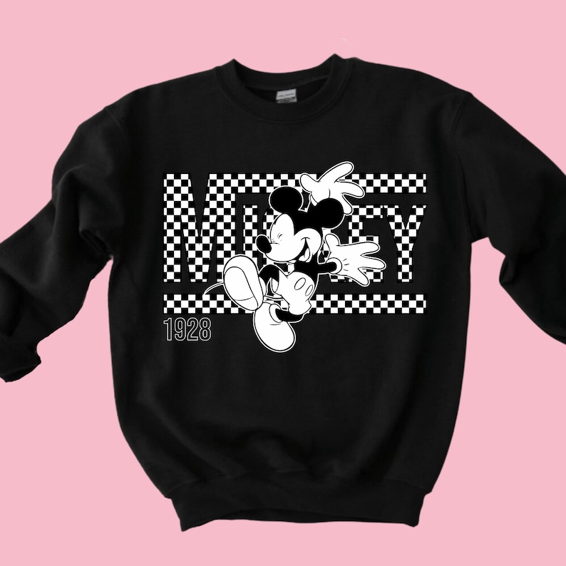 Puede incluir: Sudadera negra con un dise&ntilde;o a cuadros blancos y una imagen en blanco y negro de Mickey Mouse. El texto "Mickey" est&aacute; escrito en letras blancas con un contorno negro. El a&ntilde;o "1928" est&aacute; escrito en blanco debajo de la imagen.
