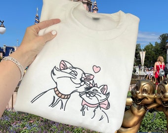 May include: White sweatshirt with a black and white embroidered image of two cats kissing. The cats are wearing pink collars and bows. A pink heart is above the cats.