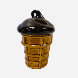 May include: A ceramic ice cream cone shaped container with a brown glaze on the top and a yellow glaze on the bottom.