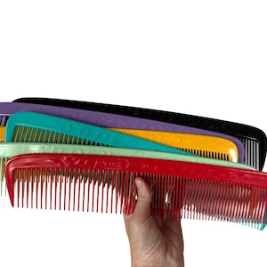May include: A stack of colorful plastic combs with the word "Super Comb" embossed on each one. The combs are arranged in a rainbow pattern, with the red comb on the bottom and the purple comb on the top.