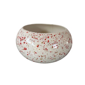 May include: White ceramic planter with a speckled red and gold design. The planter is round and has a wide opening.