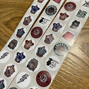 May include: A series of circular stickers on strips, with designs and text related to a popular fantasy series. Designs include crests, the Hogwarts Express logo, and the phrase "Dobby is a Free Elf." The stickers are white.