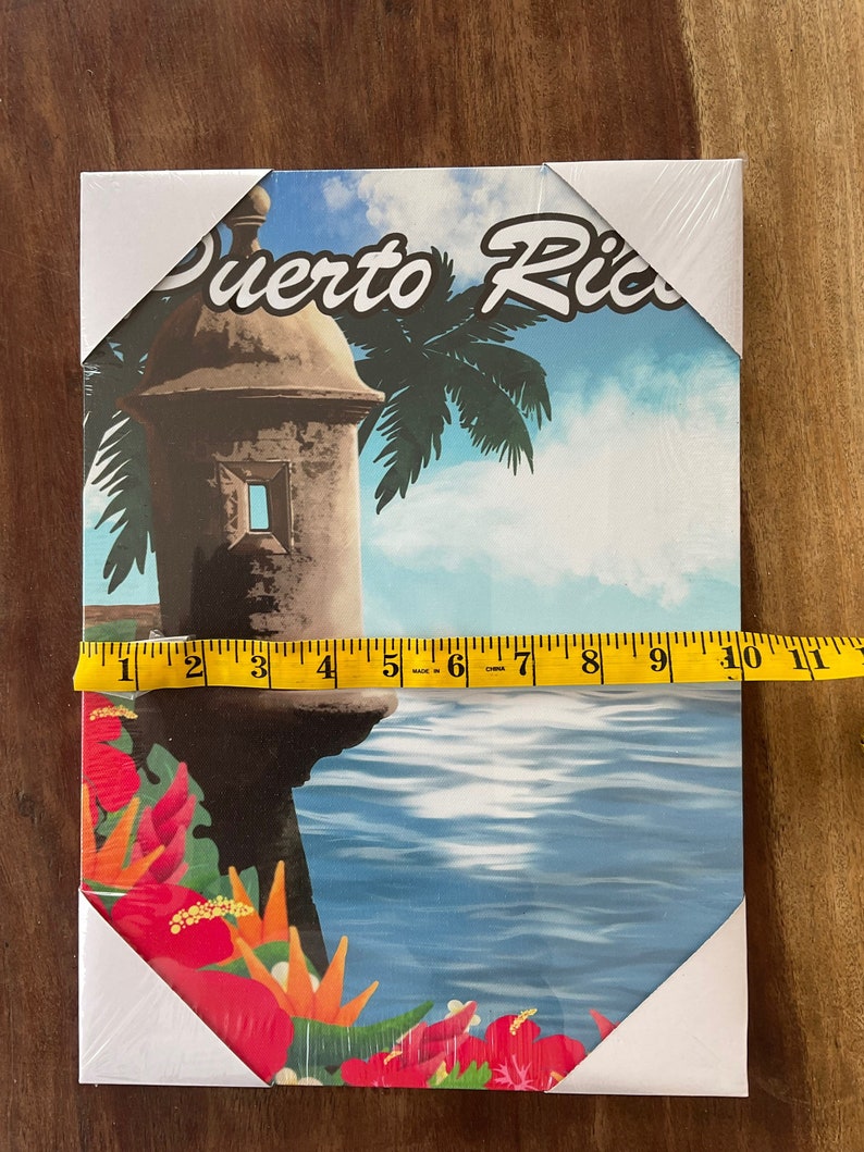 May include: A colourful canvas print featuring a vintage illustration of a stone tower with a palm tree in the background. The text "Puerto Rico" is written in a stylised font across the top of the image. The tower is situated on a cliff overlooking a blue body of water. Red flowers are in the foreground.