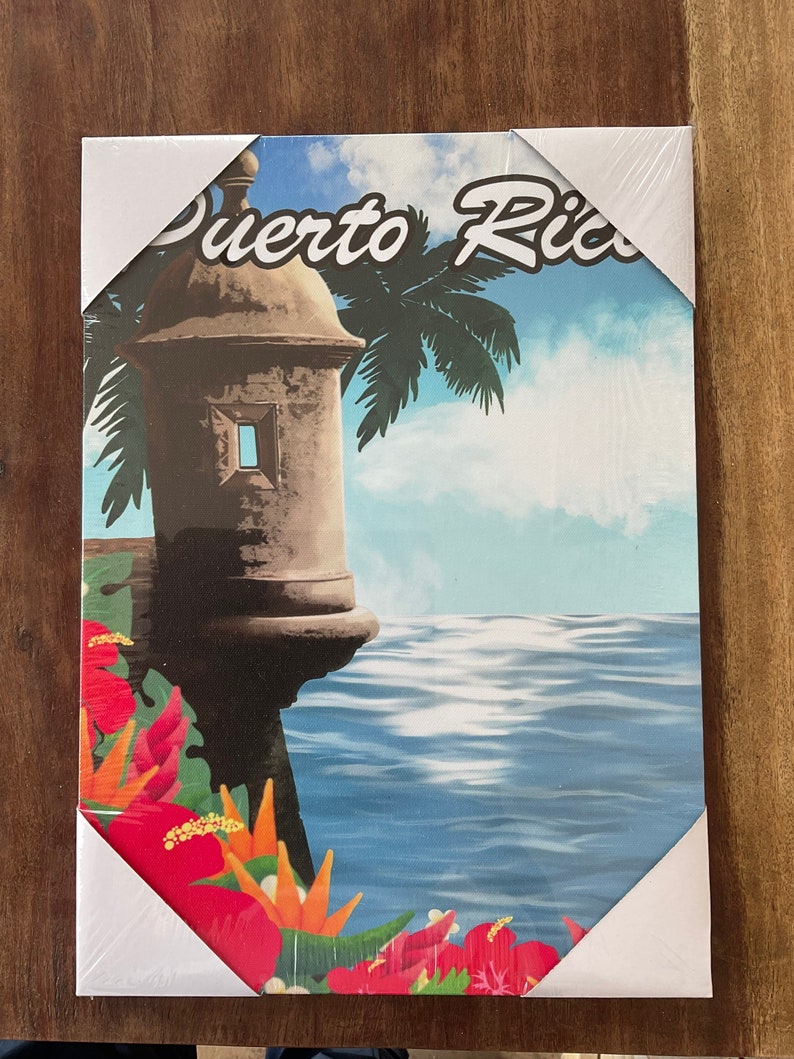 May include: A colourful canvas print featuring a stone building with a palm tree and the words "Puerto Rico" in white text. The building is situated on a cliff overlooking a blue ocean with white waves. The bottom of the print features tropical flowers in shades of red, orange, and yellow.