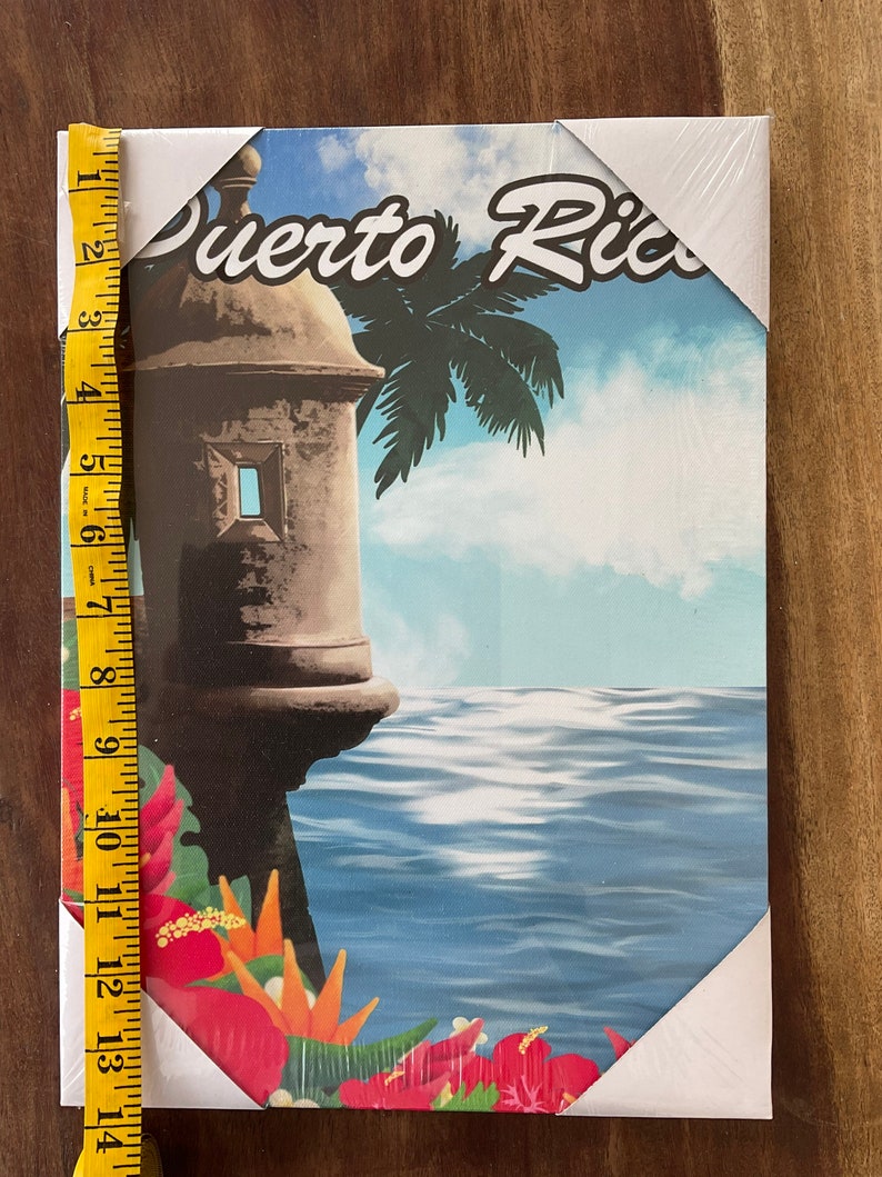 May include: A colourful canvas print featuring a view of a fort in Puerto Rico. The fort is brown and has a white window. The background shows a blue ocean, a palm tree, and a cloudy sky. The text "Puerto Rico" is written in a white, stylised font.