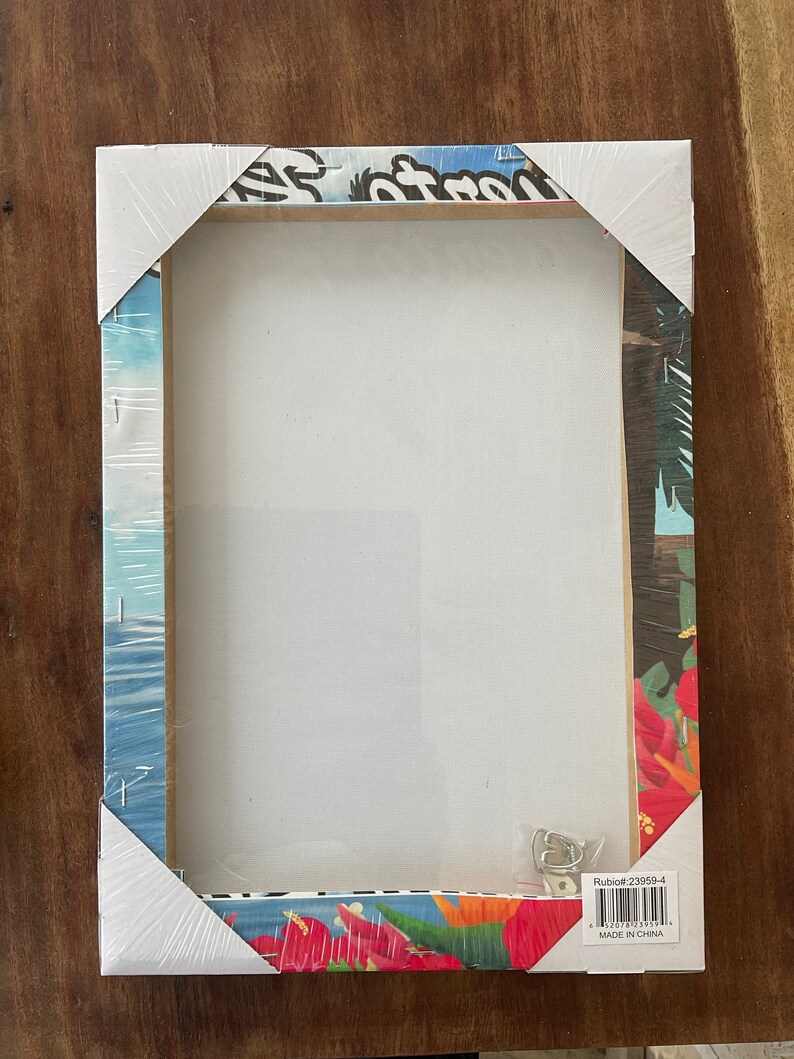 May include: A white canvas print with a tropical design. The print features a blue sky, palm trees, and red flowers. The print is wrapped around a wooden frame and has a hanging hook on the back. The print is packaged in a clear plastic bag with a label that says "Rubioff #23959-4" and "Made in China".