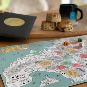 May include: A colourful board game featuring a map of Cornwall, England. The game includes various activities and landmarks, such as a cream tea, fishing, and a castle. Players can explore the region and discover its culture and cuisine.