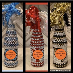 May include: Three decorative glass bottles with rhinestones and a custom design option. The bottles are decorated with blue, red, and gold ribbons and bows. The bottles have a clear glass base and a silver top. The bottles are decorated with rhinestones in a pattern that resembles a team logo. The bottles have a label that says "Custom Design your Logo".