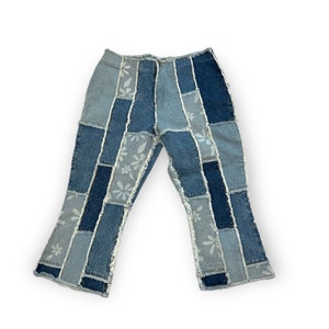 May include: Blue denim jeans with a patchwork design and white floral print. The jeans have a flared leg and raw edges.
