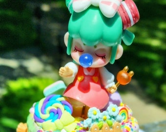 Puede incluir: Un pastel de dos pisos decorado con chispas de colores, caramelos y una pequeña muñeca con cabello verde y un lazo rosa. El pastel está cubierto con un arcoíris, una cerca y una escalera.