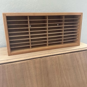 May include: A rectangular wooden organizer with multiple horizontal shelves and vertical dividers. The natural wood finish has a light brown color. The organizer is designed to hold small items and is suitable for home or office use.