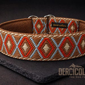 Könnte beinhalten: Ein braunes Hundehalsband mit einem sich wiederholenden Rautenmuster aus orangefarbenem, hellblauem und cremefarbenem Garn. Das Halsband hat ein schwarzes Stoffetikett mit der weißen Aufschrift deroi-collars und zwei silberfarbene Metallringe.