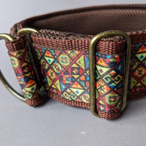 May include: A brown pet collar featuring a vibrant, multi-colored geometric pattern with triangles, squares, and circles. The collar is constructed from brown webbing with a textured interior and includes antique brass-toned metal hardware.