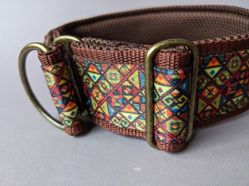 May include: A brown pet collar featuring a vibrant, multi-colored geometric pattern with triangles, squares, and circles. The collar is constructed from brown webbing with a textured interior and includes antique brass-toned metal hardware.