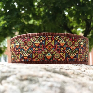 May include: A brown nylon webbing collar featuring a vibrant, multi-colored geometric pattern of triangles, diamonds, and squares in shades of red, yellow, blue, and green, with a textured weave and a sturdy, flat, cylindrical construction.