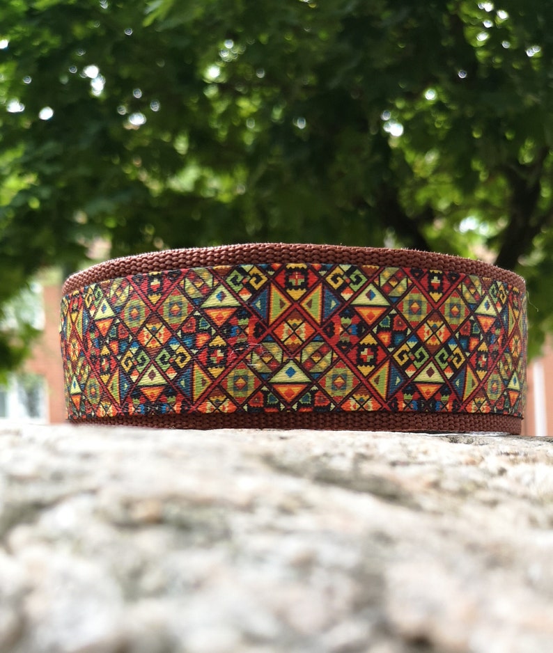 May include: A brown nylon webbing collar featuring a vibrant, multi-colored geometric pattern of triangles, diamonds, and squares in shades of red, yellow, blue, and green, with a textured weave and a sturdy, flat, cylindrical construction.