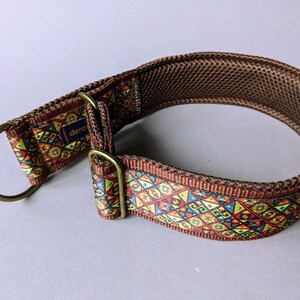 May include: A brown dog collar featuring a vibrant, multi-colored geometric pattern on the outer strap. The collar includes a brass-toned metal D-ring and an adjustable slider, with a dark brown mesh lining on the interior and a small black tag.