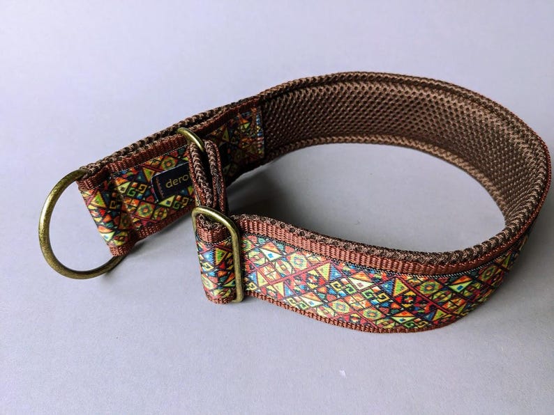 May include: A brown dog collar featuring a vibrant, multi-colored geometric pattern on the outer strap. The collar includes a brass-toned metal D-ring and an adjustable slider, with a dark brown mesh lining on the interior and a small black tag.