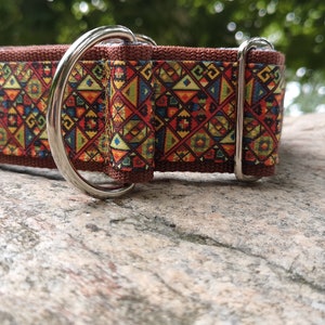 May include: A brown fabric pet collar featuring a repeating geometric pattern in shades of red, yellow, blue, and green. The collar includes a silver-toned metal D-ring for attachment and a matching silver-toned metal sliding buckle for size adjustment.