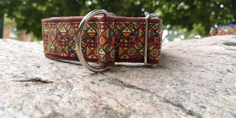 May include: A brown fabric pet collar featuring a repeating geometric pattern in shades of red, yellow, blue, and green. The collar includes a silver-toned metal D-ring for attachment and a matching silver-toned metal sliding buckle for size adjustment.
