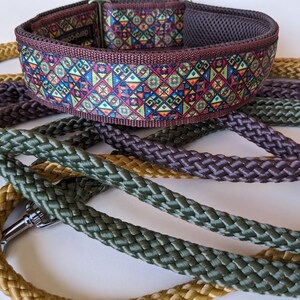 May include: A wide dog collar featuring a colorful geometric pattern in shades of blue, red, yellow, and green, with a dark brown mesh lining. It is accompanied by several braided leashes in solid olive green, mustard yellow, and dark brown.