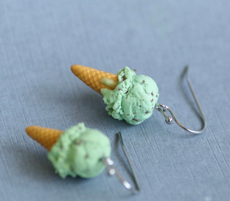 Puede incluir: Un par de pendientes originales con forma de conos de helado en miniatura. Cada pendiente tiene un cono marr&oacute;n claro rematado con una bola de helado verde menta con motas oscuras. Los pendientes tienen ganchos para la oreja de color plateado.