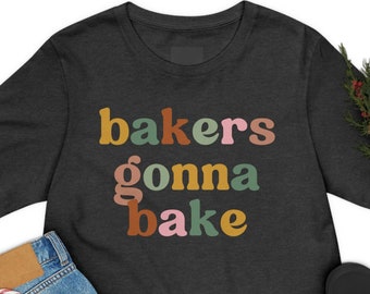 Peut inclure: Un t-shirt gris foncé avec le texte "bakers gonna bake" en lettres colorées. Les lettres sont dans une police de caractères de style rétro.