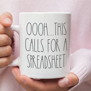 Könnte beinhalten: Eine weiße Keramik-Kaffeetasse mit schwarzem Text, der "OOOH... THIS CALLS FOR A SPREADSHEET" lautet.