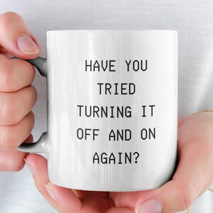 May include: White ceramic mug with black text that reads "Have you tried turning it off and on again?"