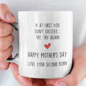 May include: White ceramic mug with black text that reads "If at first you don't succeed... try, try again. Happy Mother's Day. Love your second born." A small red heart is above the text "Happy Mother's Day".