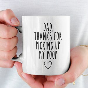 Op de afbeelding: Witte keramische koffiemok met zwarte tekst die "Papa, bedankt voor het opruimen van mijn poep" zegt met een klein hartje onderaan.