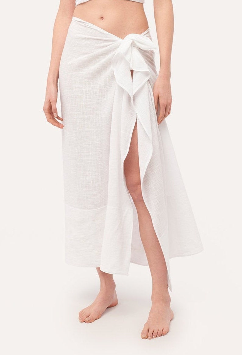 May include: A white cotton sarong skirt with a side slit and a knotted tie at the waist.