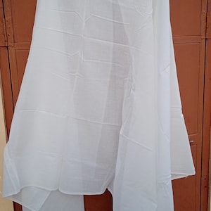 May include: A white sheer scarf hanging on a hanger against a brown wooden door.