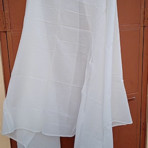 May include: A white sheer fabric scarf hanging on a brown door. The scarf is folded in half and has a smooth texture.