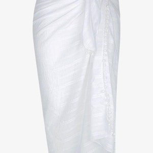 May include: White cotton sarong with a pom-pom trim. The sarong is tied at the waist and has a flowing, relaxed fit.