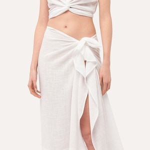 May include: A white cotton wrap skirt with a side slit and a knotted tie at the waist.